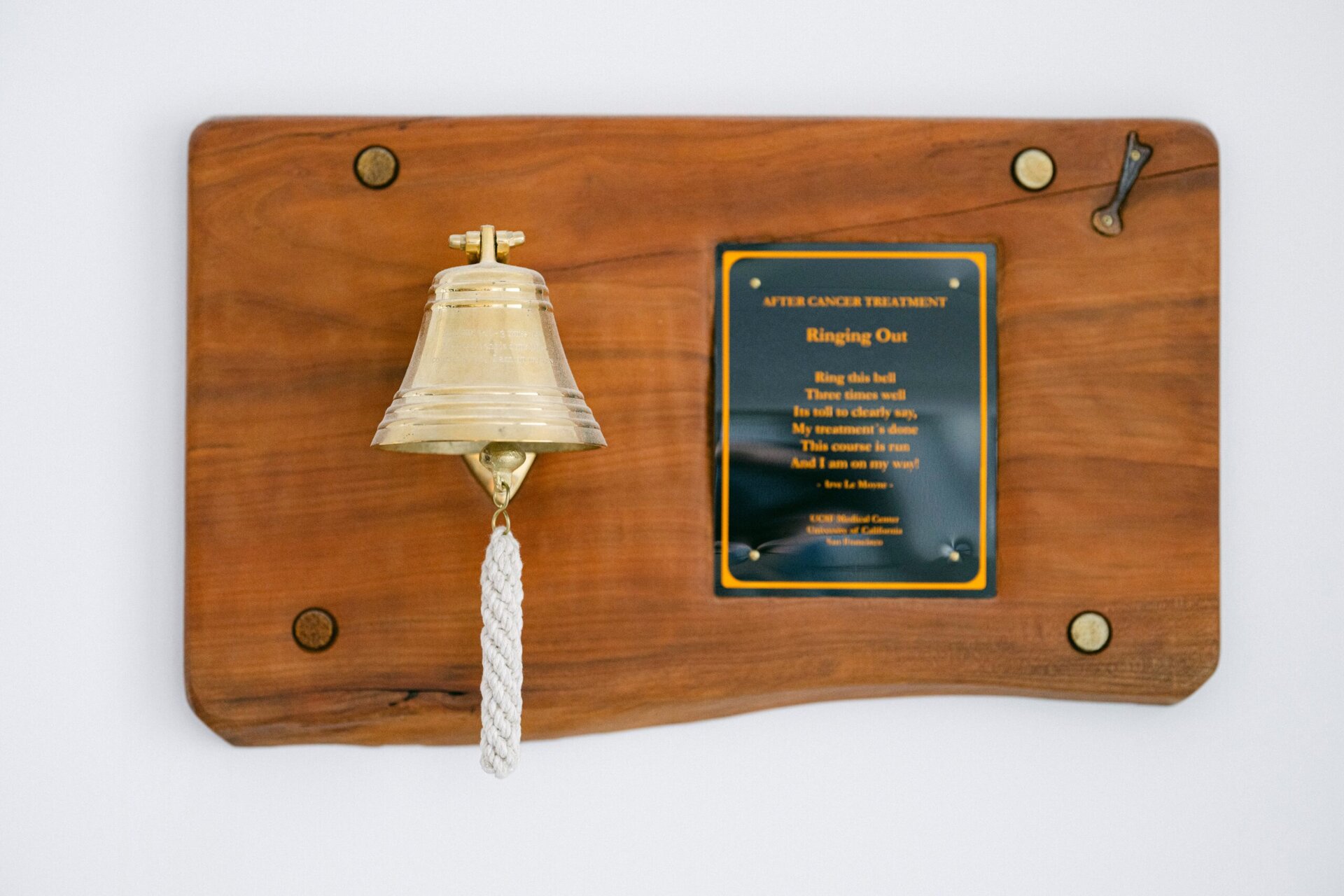 Eine Plakette mit einem Motivationsspruch ist zu sehen. Daneben befindet sich eine Glocke, die geläutet wird, wenn ein Patient die Krebsbehandlung positiv überstanden hat.